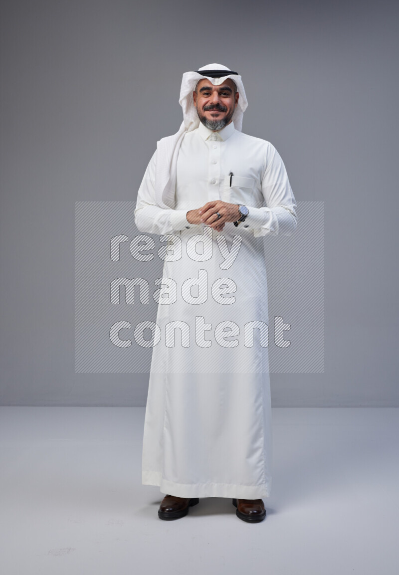 Saudi man Wearing Thob and white Shomag standing interacting with the camera on Gray background