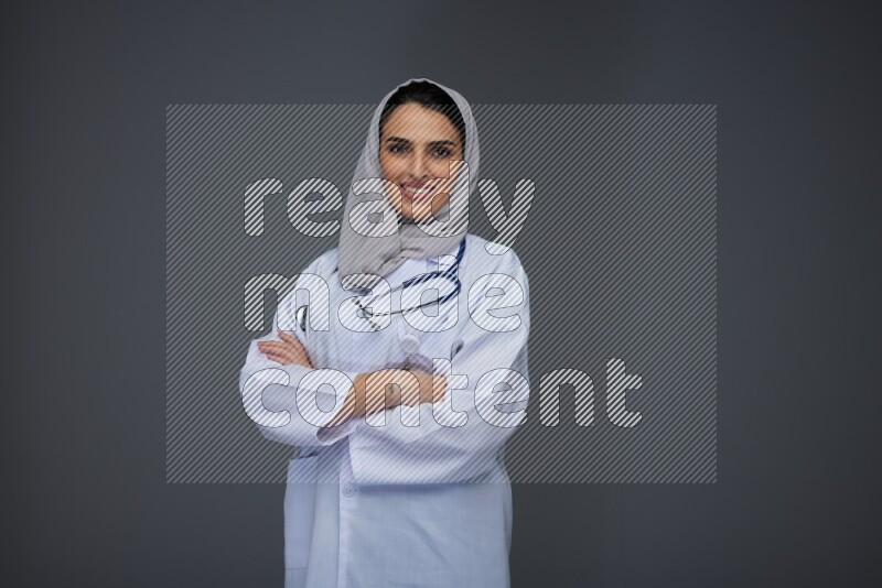 A female doctor wearing a light gray head scarf standing on grey background.