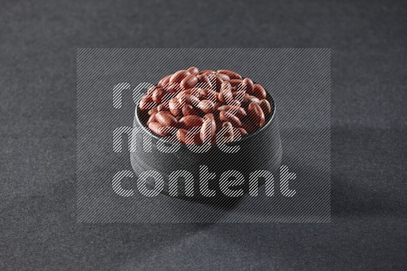 A black pottery bowl full of red skin peanuts on a black background in different angles