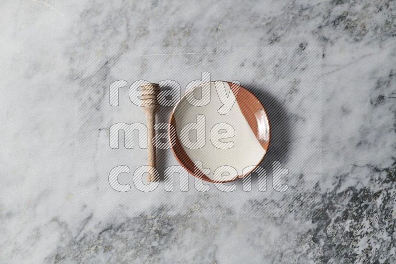 Multicolored Pottery Plate with wooden honey handle on the side on grey marble flooring, Top view