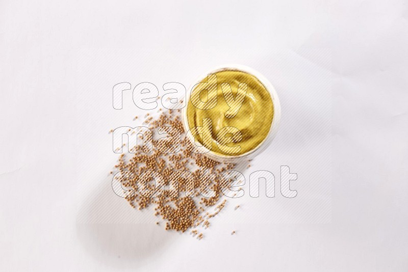 A beige pottery bowl full of mustard paste with mustard seeds underneath on white flooring in different angles