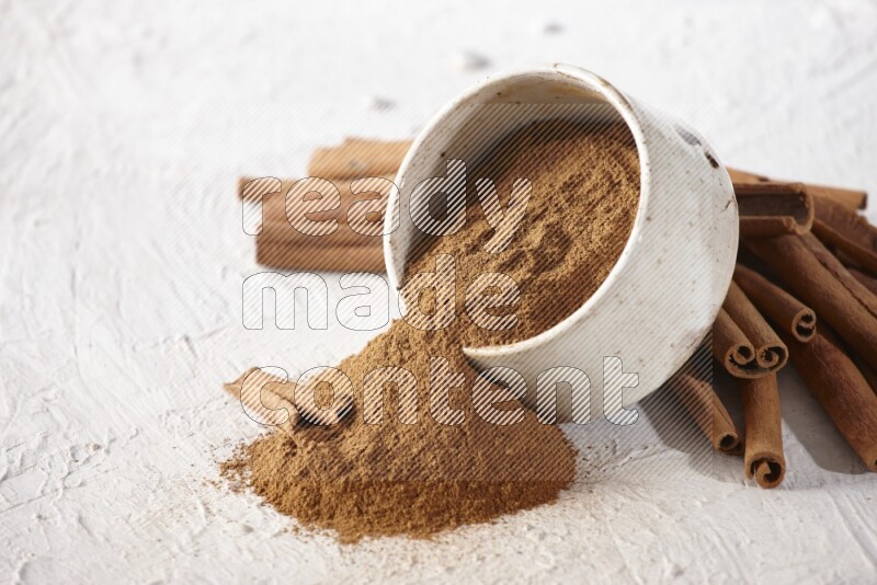 Ceramic beige bowl over filled with cinnamon powder and cinnamon sticks around the bowl on a textured white background in different angles
