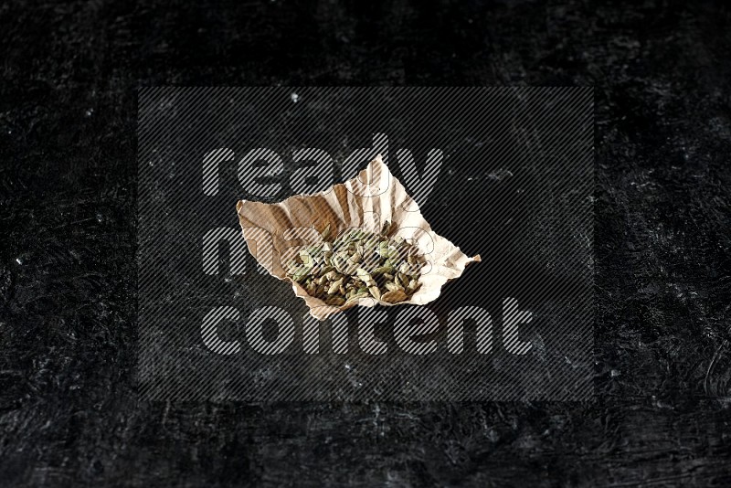 Cardamom seeds in a crumpled piece of paper on textured black flooring