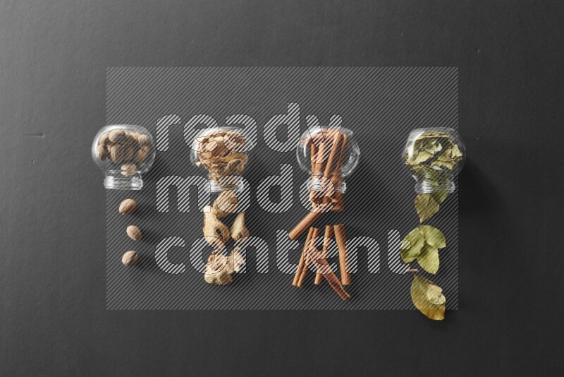 أوراق الغار وزنجبيل مجفف وقرفة وجوزة الطيب في أوعية زجاجية علي خلفية سوداء