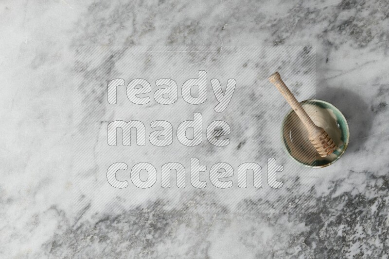 Multicolored pottery bowl with wooden honey dipper in it on grey marble background
