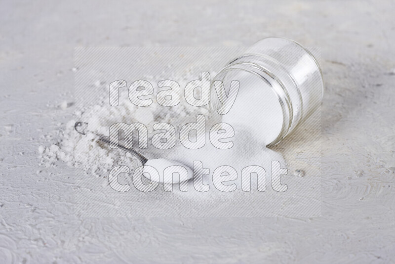 A glass jar full of table salt with some sea salt crystals beside it on a white background