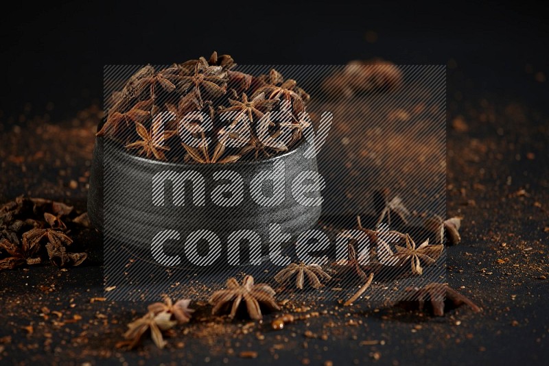 Star Anise in a black bowl with sprinkled anise on black flooring