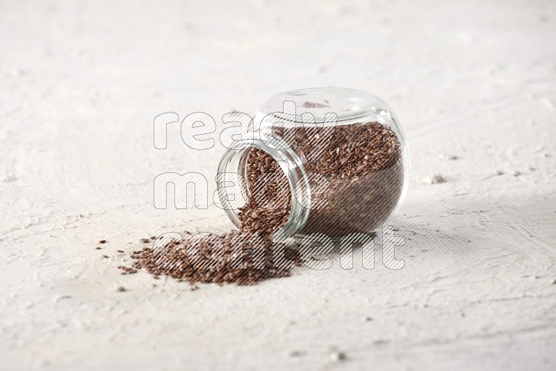 A glass spice jar full of flax flipped and flax spreaded out on a textured white flooring in different angles