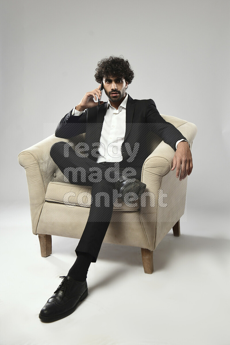 A man wearing formal sitting on a chair talking on the phone on white background