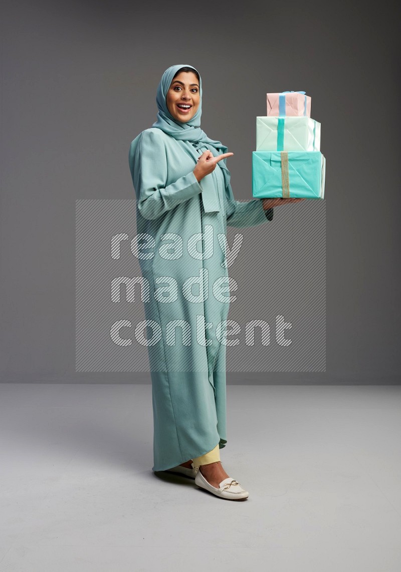 Saudi Woman wearing Abaya standing holding gift box on Gray background