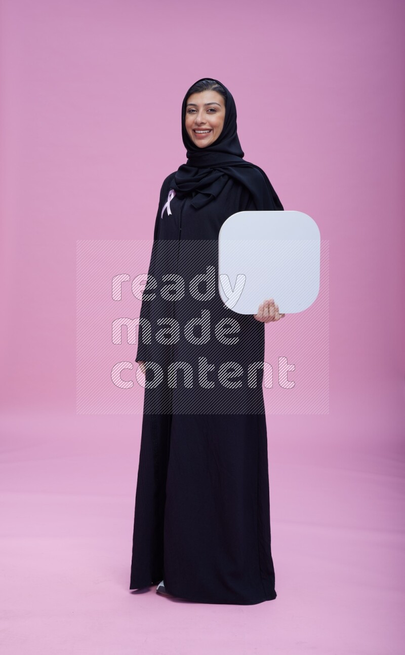 Saudi woman wearing pink ribbon on Abaya standing holding social media signs on pink background