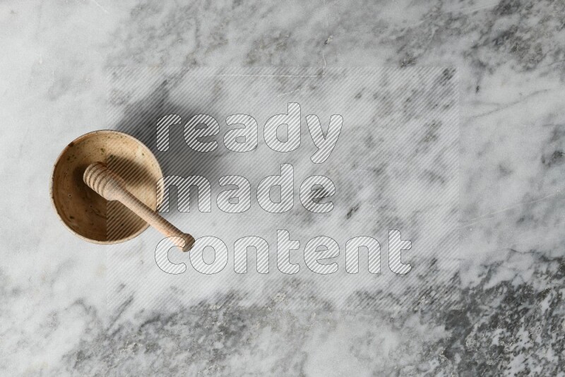 Beige pottery bowl with wooden honey dipper in it on grey marble background