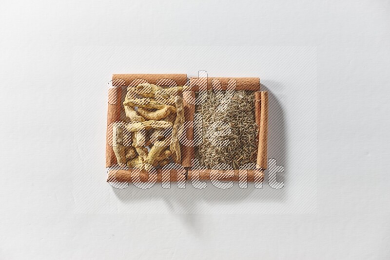 مربعان من أعواد القرفة ممتلئان بحبوب الكمون وأصابع الكركم علي خلفية بيضاء