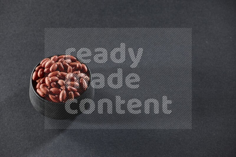 A black pottery bowl full of red skin peanuts on a black background in different angles