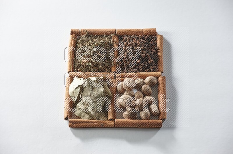 4 squares of cinnamon sticks full of bay laurel leaves, dried basil, cloves and nutmegs on white flooring