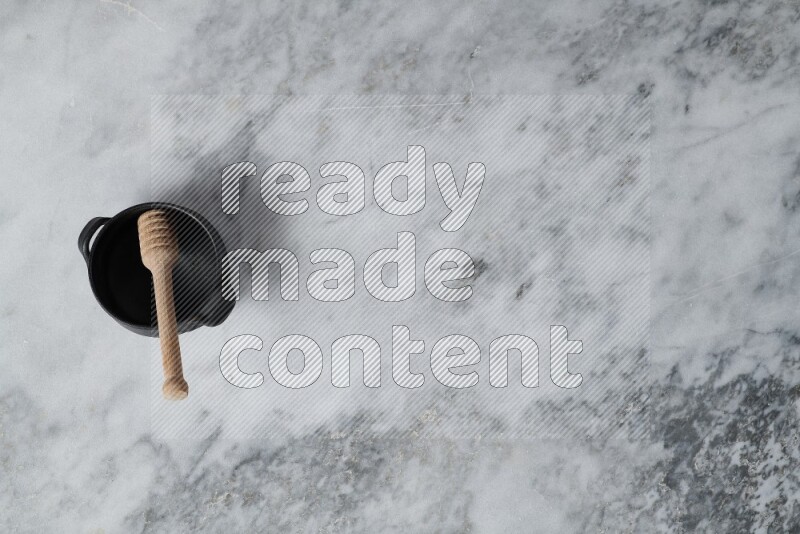 وعاء فخاري أسود مع ملعقة عسل خشبية بداخله على خلفية من الرخام الرمادي