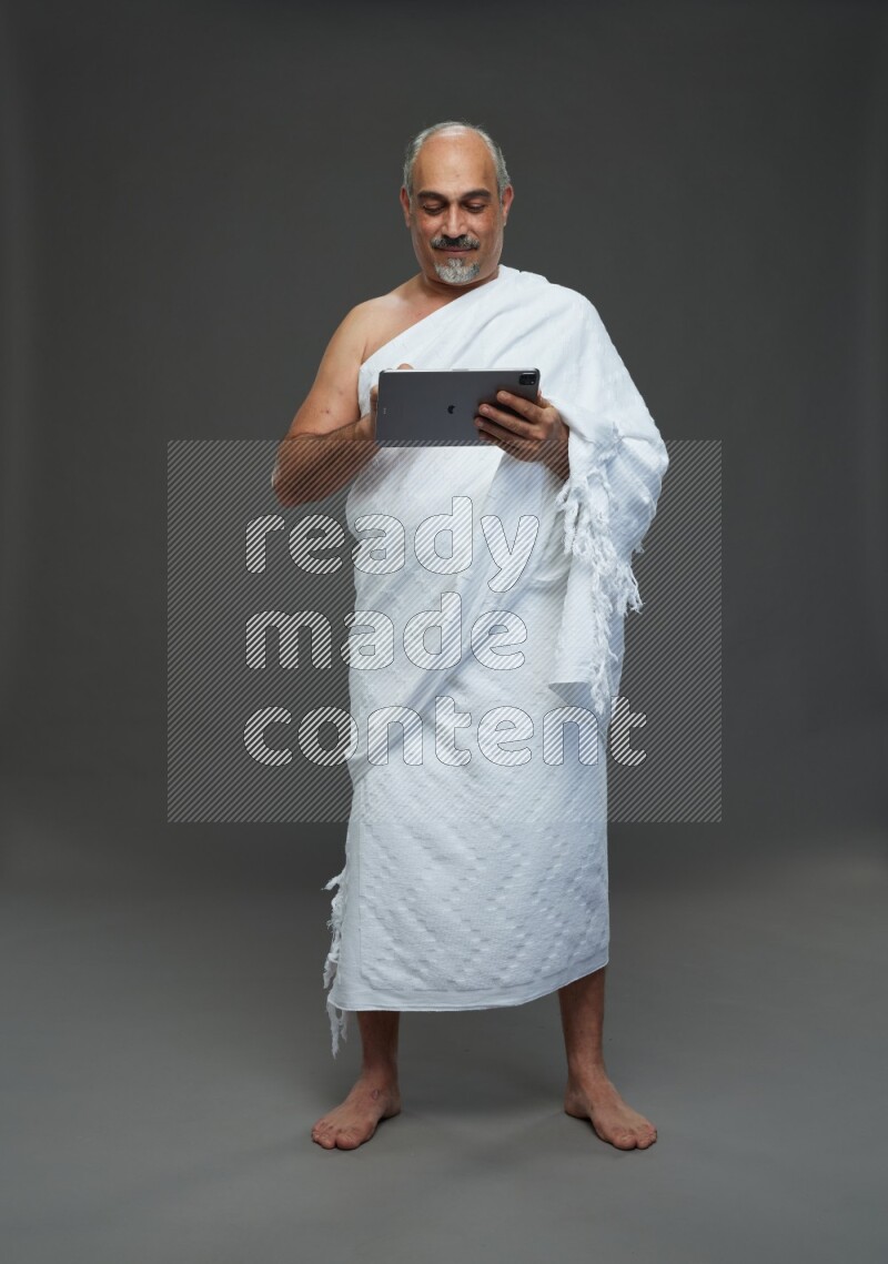 A man wearing Ehram Standing working on tablet on gray background
