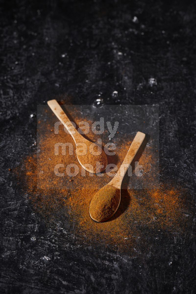 Two wooden spoons full of ground paprika powder on black background