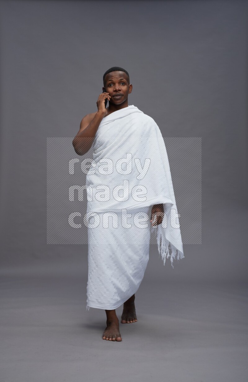 A man wearing Ehram Standing talking on phone on gray background