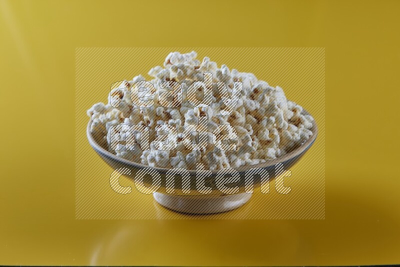 A multicolored ceramic plate full of popcorn on a yellow background in different angles