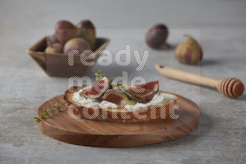 quarters of figs with cream cheese on toasted sourdough slice on a wooden board on textured grey background