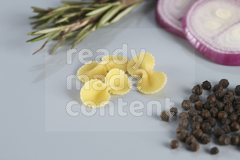 Raw pasta with different ingredients such as cherry tomatoes, garlic, onions, red chilis, black pepper, white pepper, bay laurel leaves, rosemary, cardamom and mushrooms on light blue background