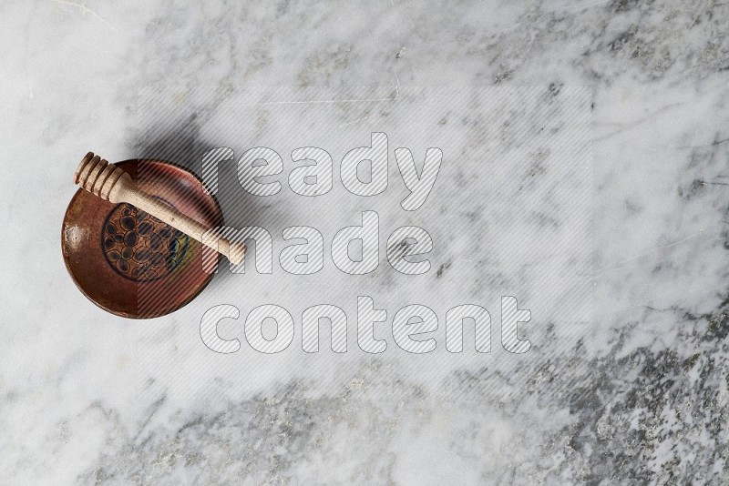 Decorative Pottery Plate with wooden honey handle in it, on grey marble flooring, Top View