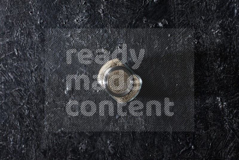 Herbal glass jar full of white pepper on textured black flooring