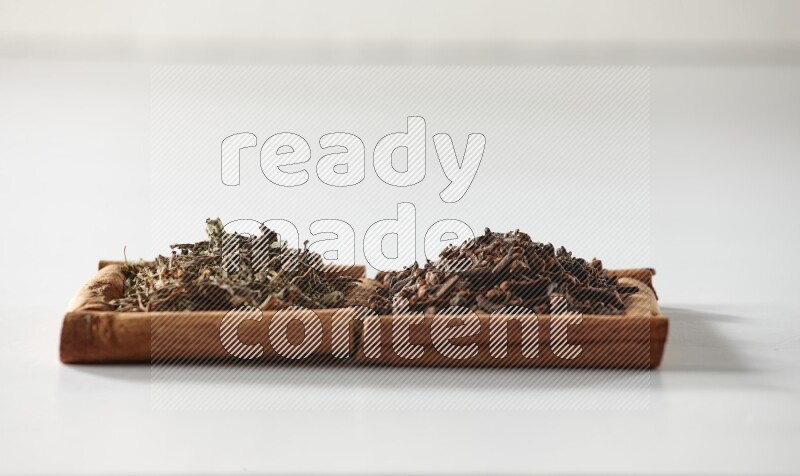 مربعان من أعواد القرفة ممتلئان بالقرنفل والريحان المجفف علي خلفية بيضاء