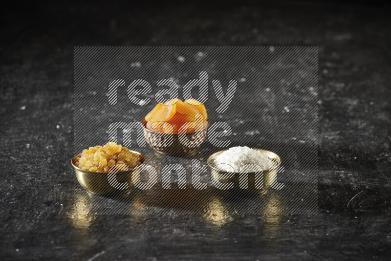 Dried fruits in metal bowls in a dark setup