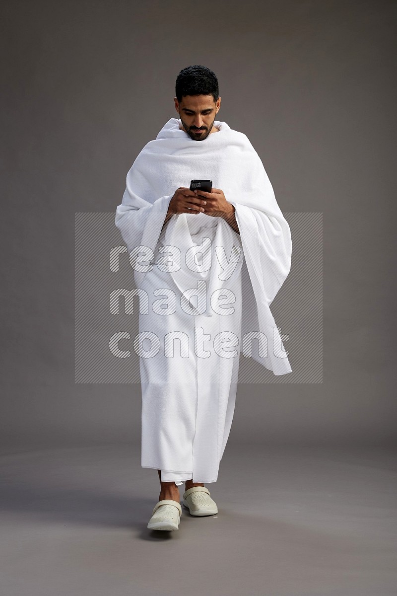 A man wearing Ehram Standing texting on phone on gray background