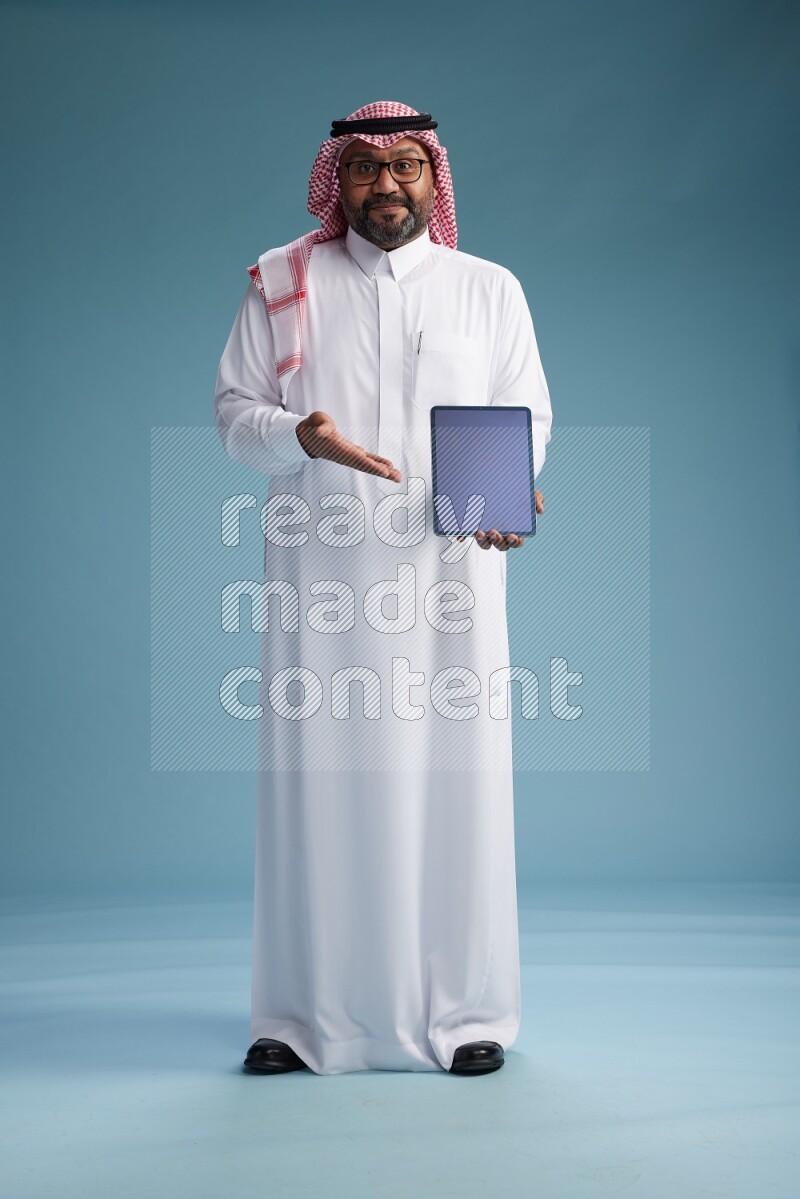 Saudi Man with shimag Standing holding a tablet on blue background