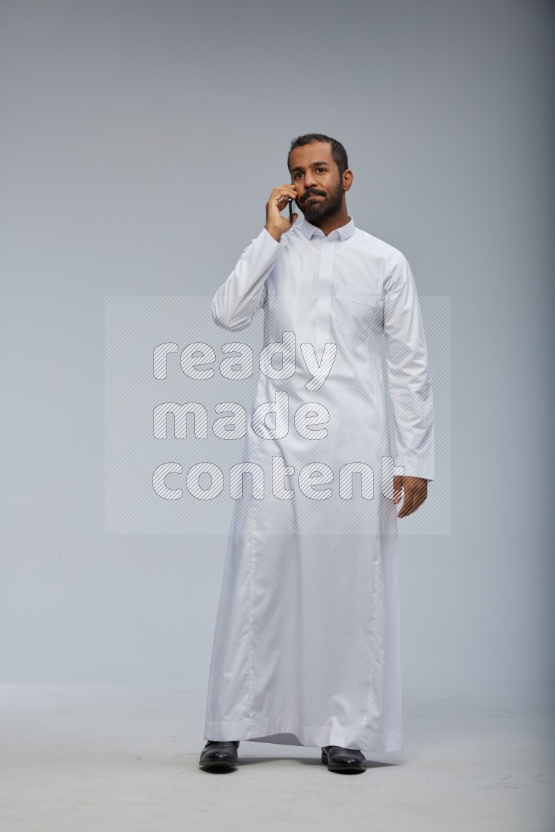 Saudi man wearing Thob standing talking on phone on Gray background