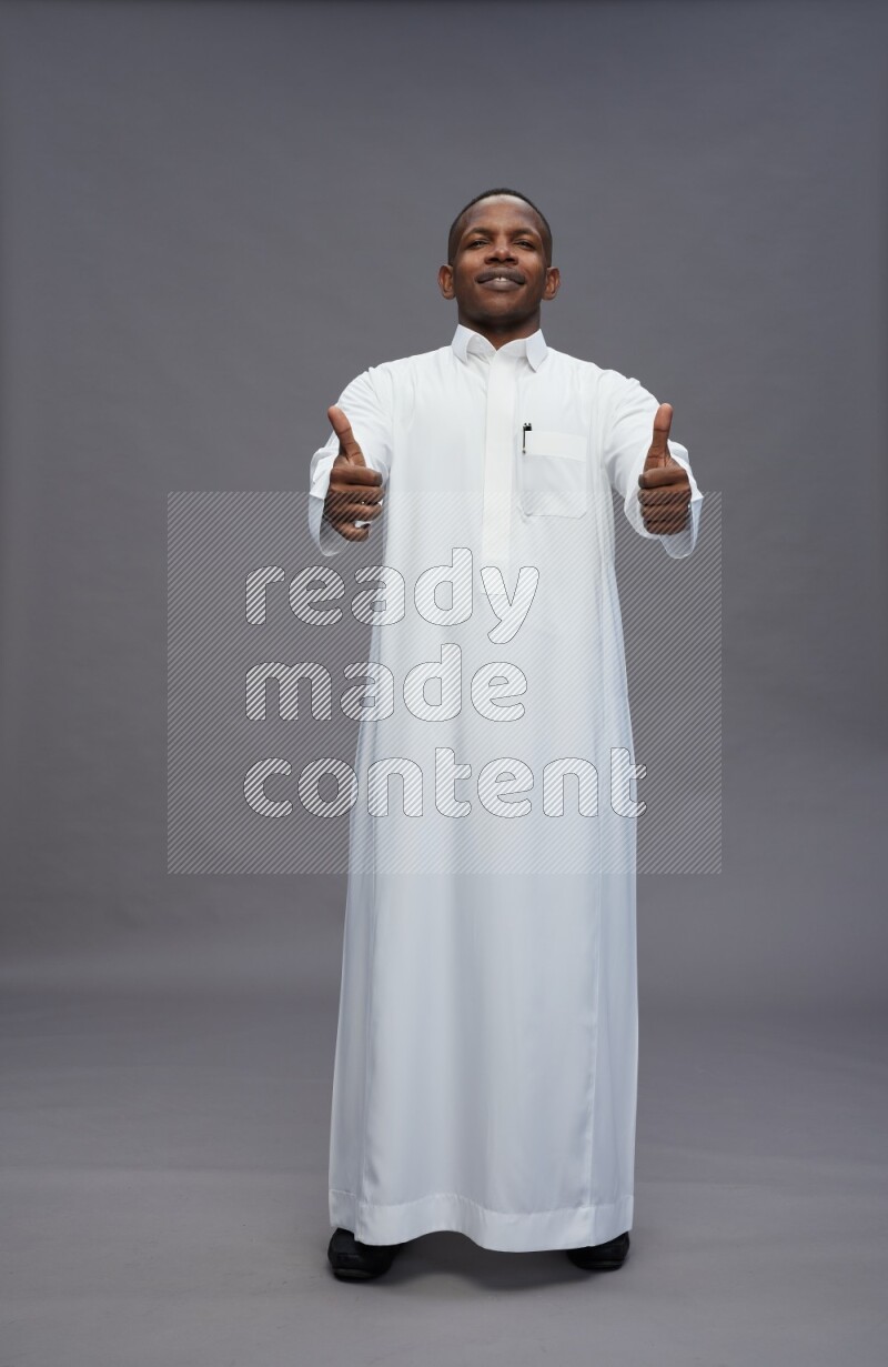 Saudi man wearing thob standing interacting with the camera on gray background