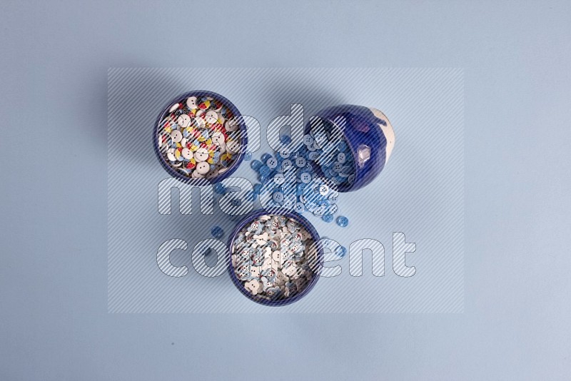 Multicolored pottery bowl full of colored buttons on blue background