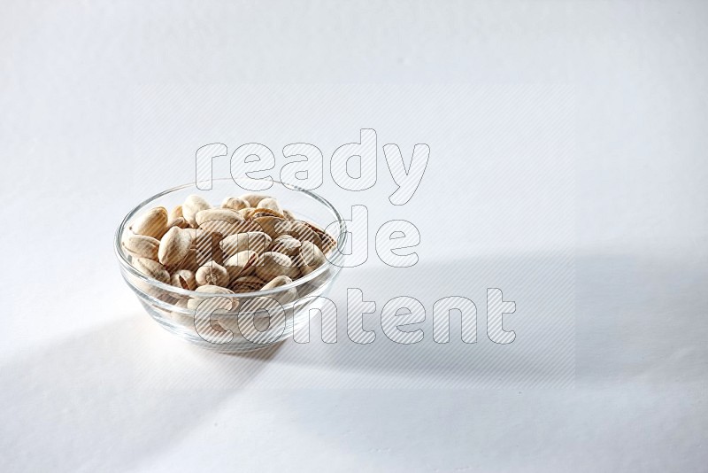 A glass bowl full of pistachios on a white background in different angles