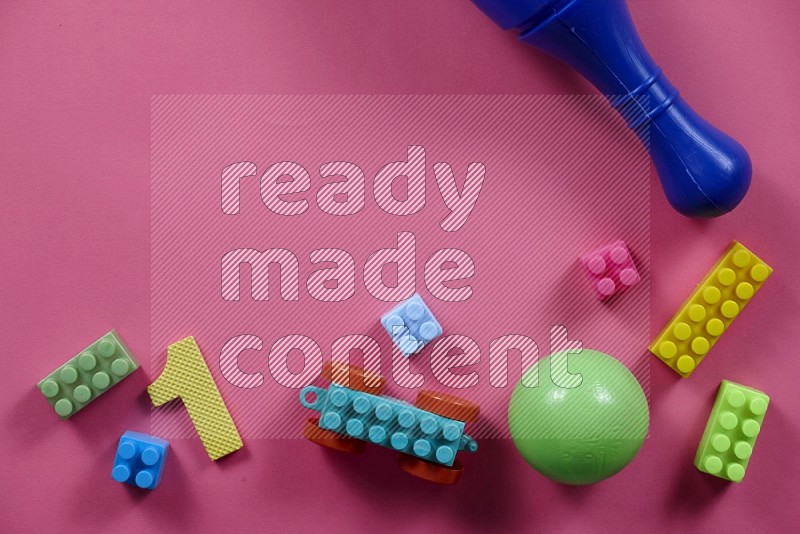 Plastic building blocks, balls and bowling pins on pink background in top view (kids toys)