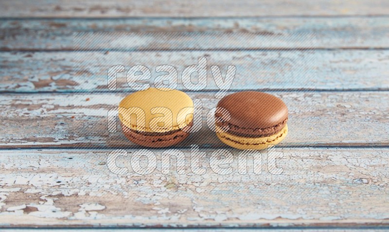 45º Shot of two Yellow and Brown Chai Latte macarons on light blue wooden background