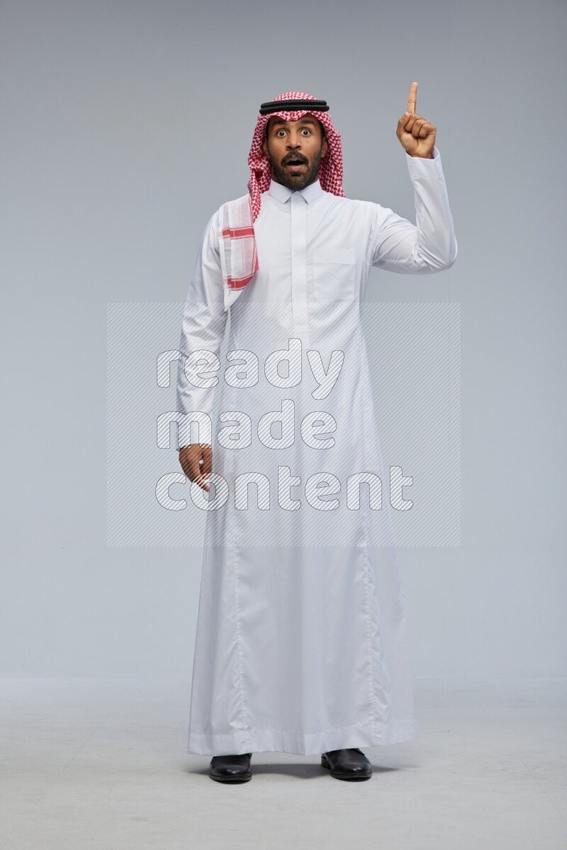 Saudi man Wearing Thob and shomag standing interacting with the camera on Gray background