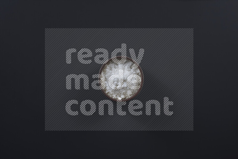 Pottery bowl full of fine table salt and coarse sea salt on black background
