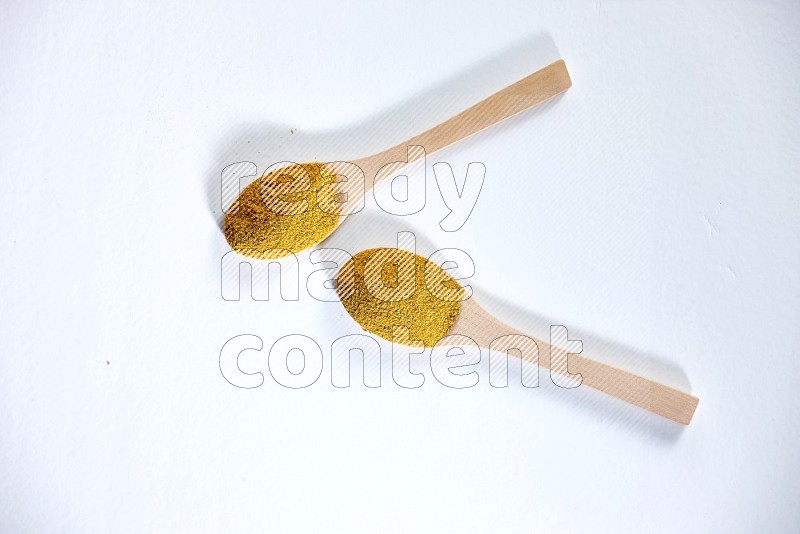 2 wooden spoons full of turmeric powder on white flooring