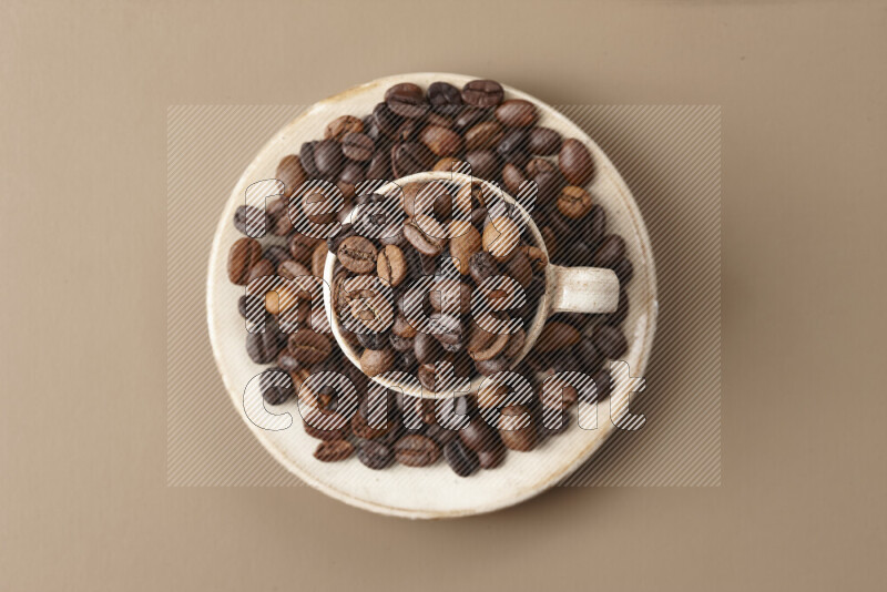 A beige pottery cup full of roasted coffee beans on beige background