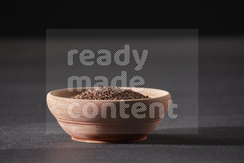 A wooden bowl full of flaxseeds on a black flooring