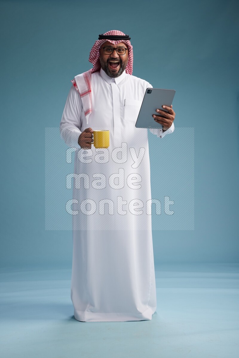 Saudi Man with shimag Standing holding a tablet on blue background