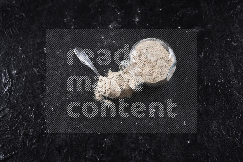 A glass jar full of onion powder flipped with some spilling powder on black background