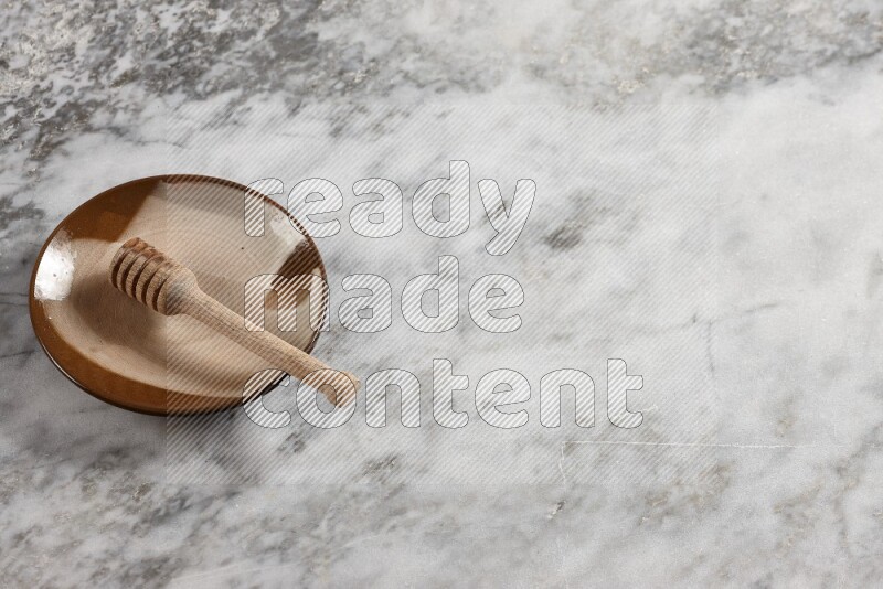 طبق فخاري متعدد الألوان مع ملعقة عسل خشبية بداخله على خلفية من الرخام الرمادي