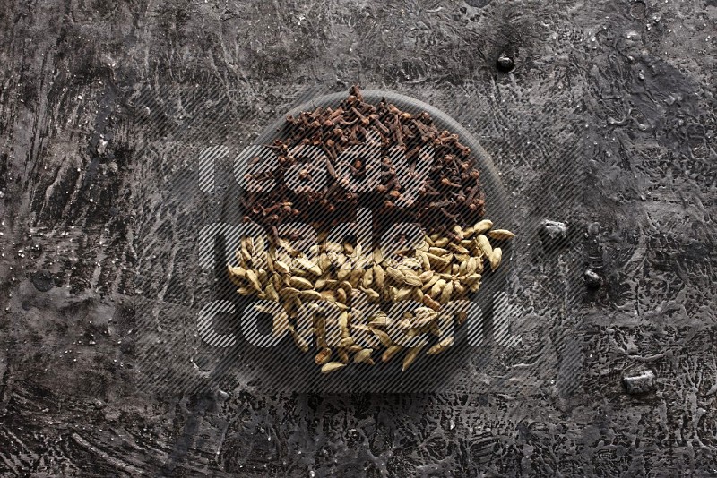 Cardamom and cloves on a black plate on textured black background