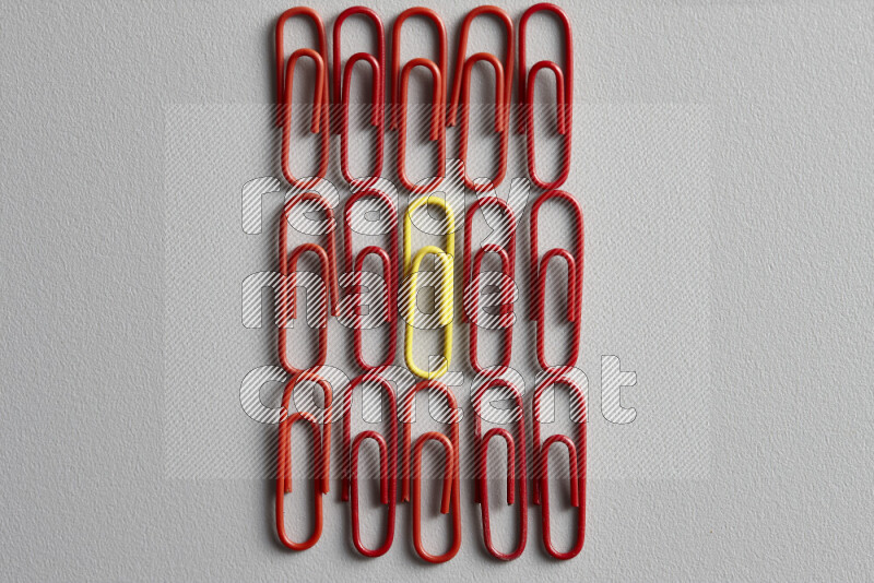 A yellow paperclip surrounded by bunch of red paperclips on grey background