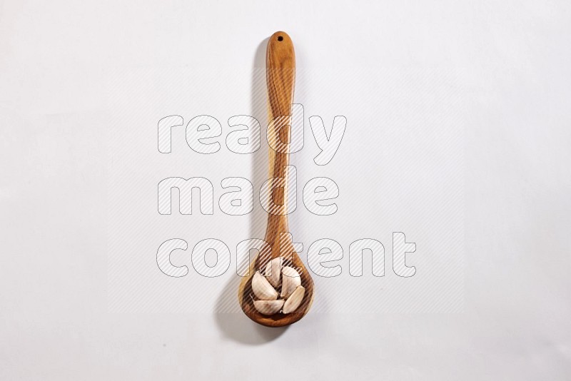 A wooden ladle full of garlic cloves on a white flooring in different angles