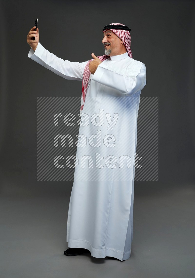 Saudi man with shomag Standing taking selfie on gray background